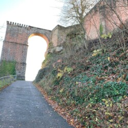 Der Burgweg führt in seinem letzten Abschnitt unterhalb der Rundbogenbrücke vorbei zur salierzeitlichen Vorburg des Trifels. Der Burgwegs zum Trifels endet am Brunnenturm